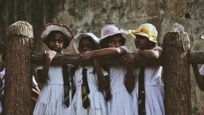four young children in school uniform stand in a row behind a wooden railing