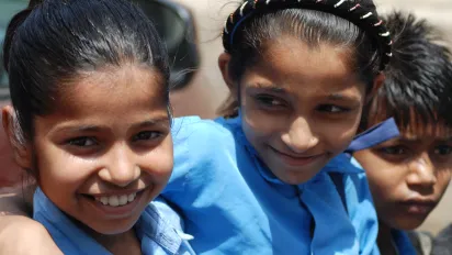 Two young girls and a young boy, smiling, wearing blue shirt uniform