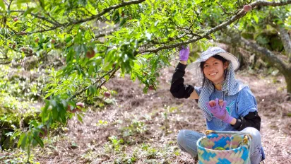 A young woman farmer under a tree holding tomatoes