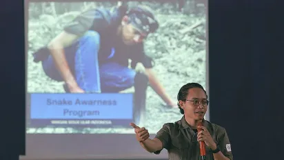 A person standing in front of a slide displaying a photo of a man with a snake