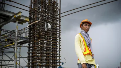 a young male construction worker in a high-rise building behind dark, cloudy skies
