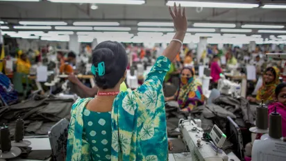 A woman stands before her colleagues with her hand raised.