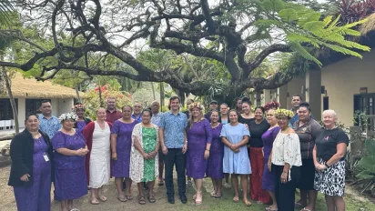 A broup of people stand under a big tree.