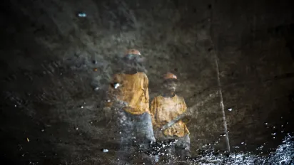 The mirrored reflection of two Malagasy construction workers captured in a puddle of water.