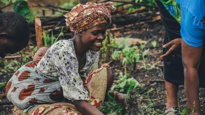 Smiling woman carrying a baby on her back, picking plants