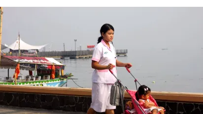 a babysitter pushing a baby cart with a toddler inside 