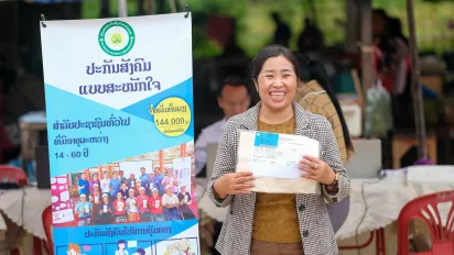 A smiling woman holding a document stands in front of a promotional standee.