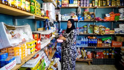 A portrait of Fatima Laanieg in her grocery store in Morocco. Food lines the shelves around her. (2025)