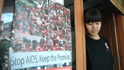 a girl in black t-shirt side by side with a poster "Stop AIDS. Keep the promise".