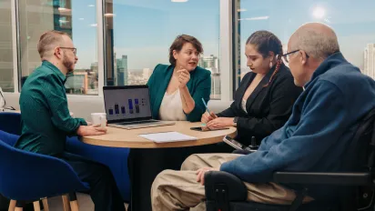 Four colleagues sitting around a table with a laptop in front of them.