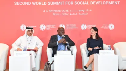 Three people sat on white chairs in formal discussion talking, two men and one woman