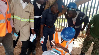 Several workers surrounding another worker, all wearing construction clothes. 