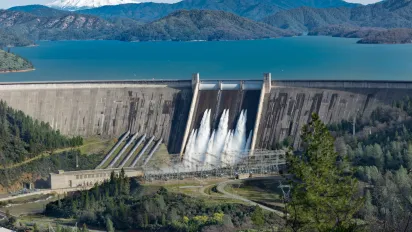 Shasta dam surrounded by roads, trees with lake mountains