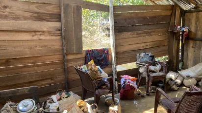 The inside of a wooden house damaged by cyclone Ditwah, with varying household items recovered from the floods gathered in different piles.