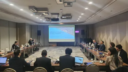 Group of people sitting at a u-shaped table in front of a screen