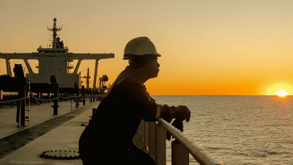 Seafarer standing at the railing of a cargo vessel, gazing at the horizon as the sun sets over the ocean
