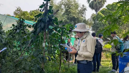 A man surrounded by plants writing in a notebook.