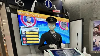 A robot in a Japanese train station interacting with the public.