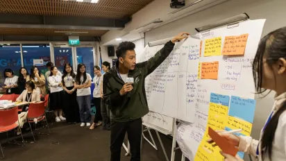 A young man pointing at a whiteboard with sticky notes during a group workshop.