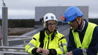 Two workers wearing helmets and yellow vests standing next to each other.