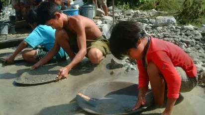three children sift gold using a heavy metal pan