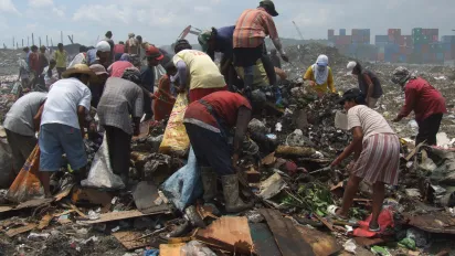 A group of people scavenging across a dumpsite, collecting items to sell or reuse for survival.