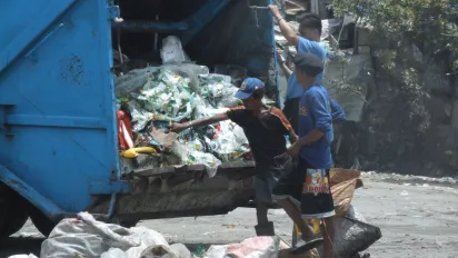 A garbage truck tipping its load of mixed waste onto a large open dumpsite.