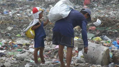 A man and a young boy scavenging side by side in a large dumpsite in Manila, surrounded by piles of garbage.