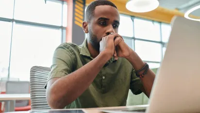 mas stressed looking at his laptop, with his hands resting on his chin.