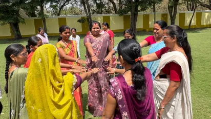 A group of women stand in a circle outdoors with their hands extended toward the center.