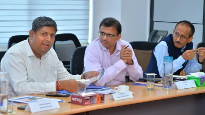 Three participants sit at a meeting table.