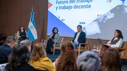 Panel sobre “Futuro del trabajo y trabajo decente” durante un evento de la OIT en Argentina. Cuatro panelistas conversan sentados sobre el escenario, junto a una bandera argentina y frente a una pantalla con la identidad visual del encuentro. En primer plano se observa al público asistente.