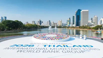 View of Bangkok’s skyline and a lake, with a circular display of international flags and signage for the 2026 IMF and World Bank Annual Meetings in the foreground.
