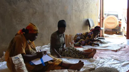 Three women sorting and recording coffee beans at a coffee processing facility.