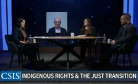 2 women and a man sitting at a table and one man on screen