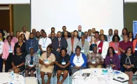 A large group of workshop participants, men and women of diverse ages pose together for a group photo in a conference room