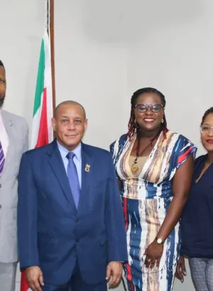 A group of people in a room standing in front of a Surinamese flag