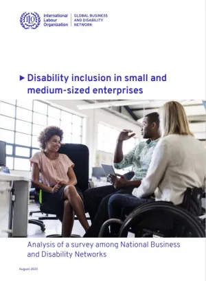 Three colleagues sitting in an office. One has short curly brown hair and is wearing a pink shirt with a black skirt. One is wearing a green checkered shirt with black pants. One is using a wheelchair and wearing a white shirt with jeans. 