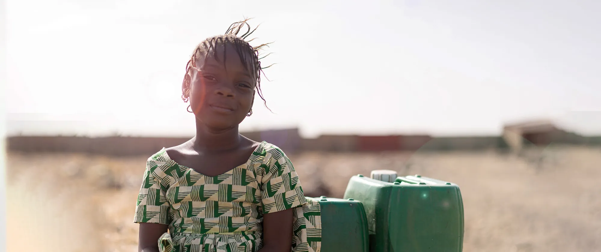 A young girl dressed in green sitting next to two green bottles of water