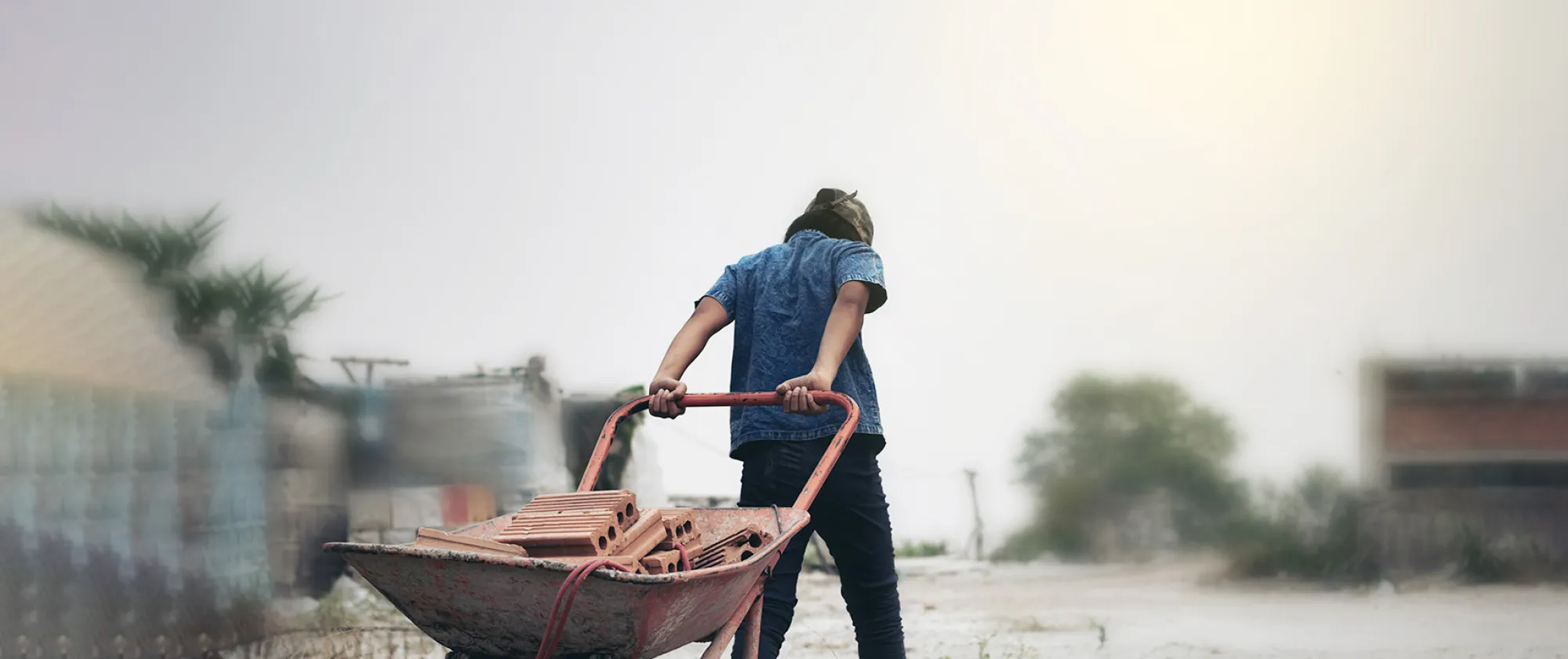 A young male child labourer pulling bricks in a wheel barrow