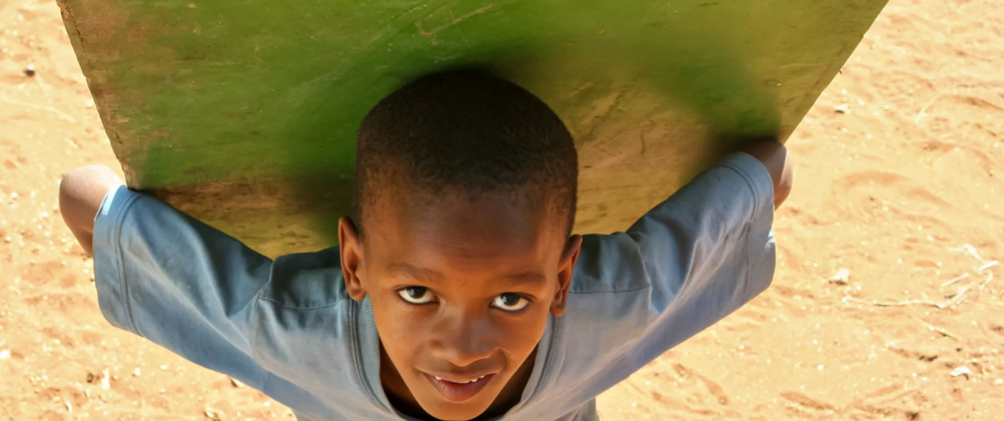 A young child labourer bent over carrying a green wooden door on his back