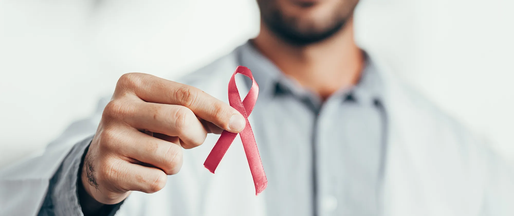 A doctor holding a red ribbon for HIV awareness between two fingers