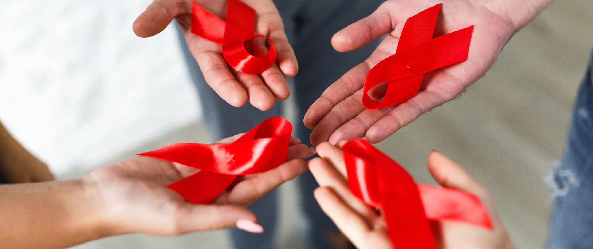 A group of young multiracial woman with red HIV/AID ribbons in the palm of their hands