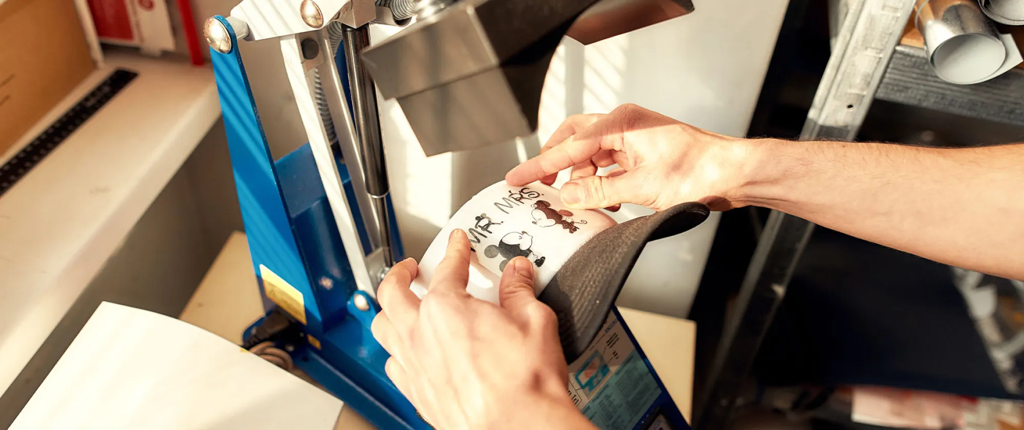 Photo of man using machine for printing image on baseball cap in workshop