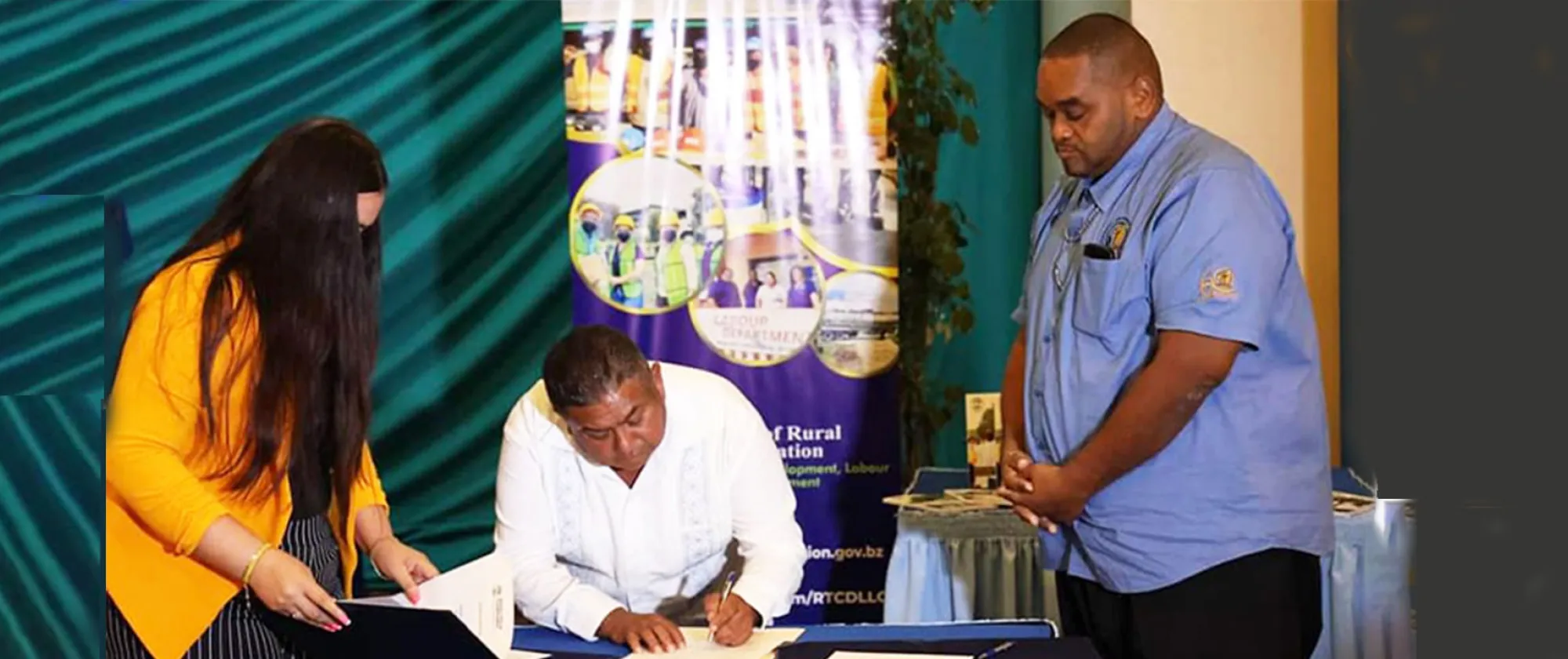 A man bent over a table signing a document while two people look on