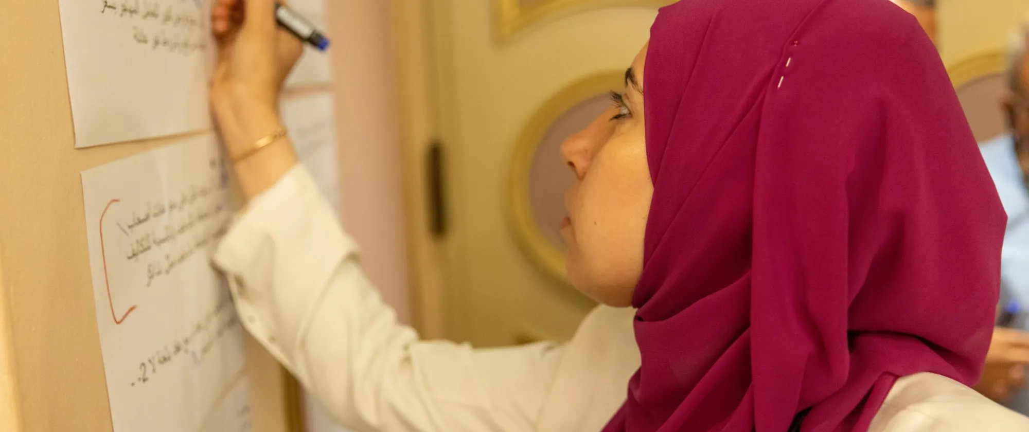 A veiled woman writing on a white board.