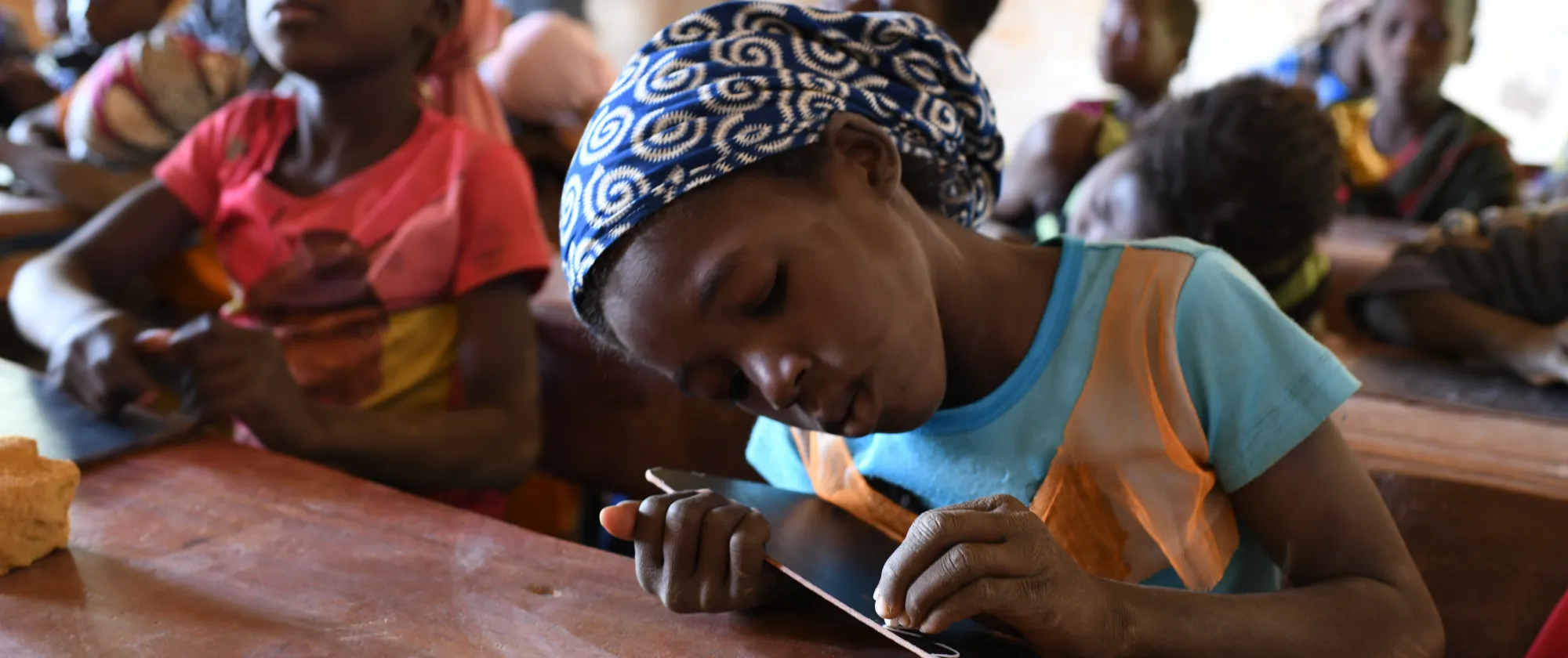 A young girl in school is writing on her slate