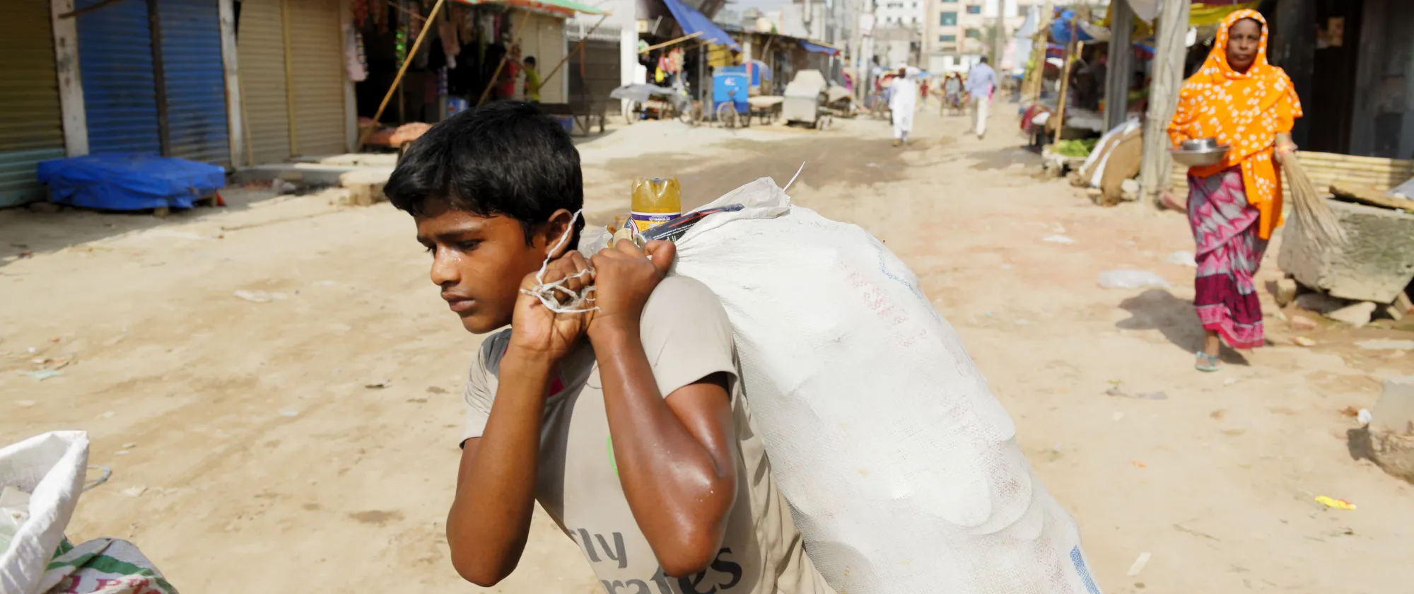 A child carries a bag across an unpaved road on the outskirts of the capital Dhaka, Bangladesh.