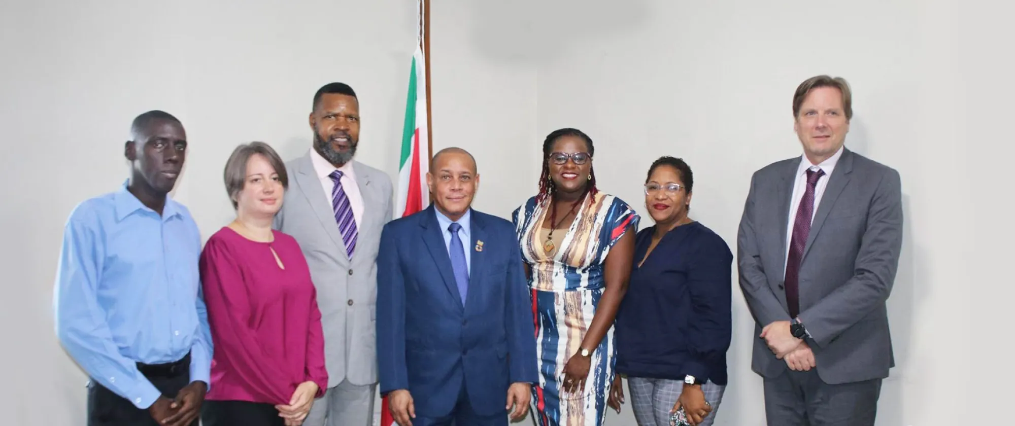 A group of people in a room standing in front of a Surinamese flag