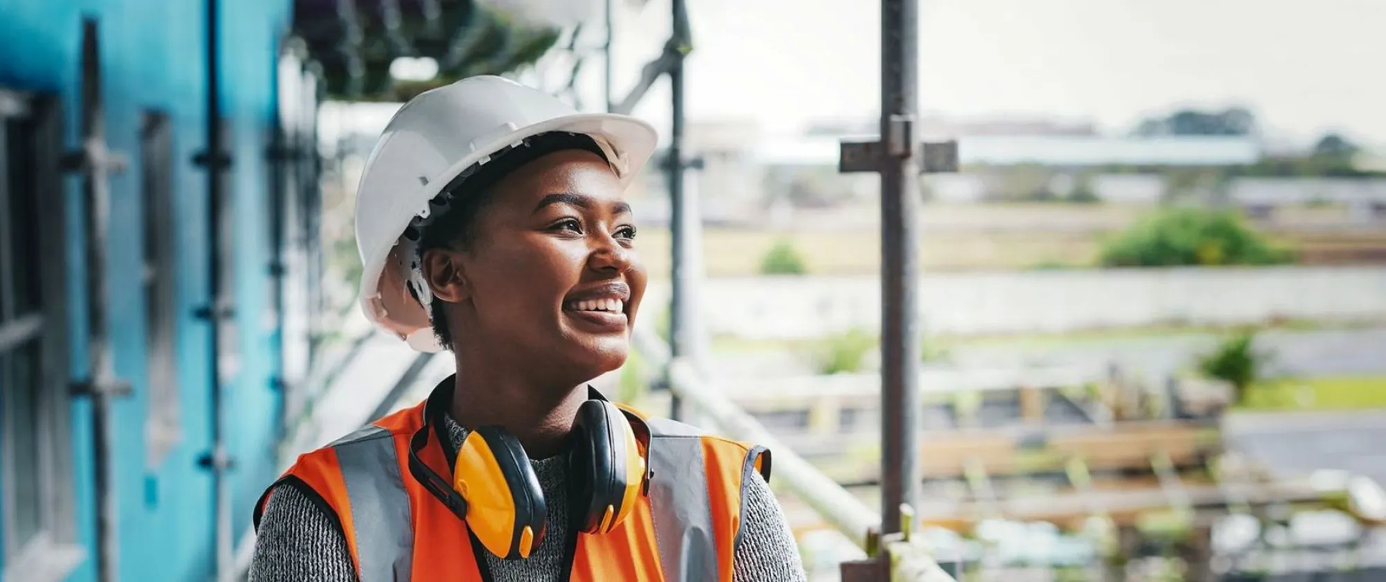 A happy, smiling and cheerful young woman or senior construction industry worker standing at a building site